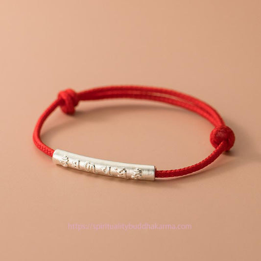Handgefertigtes Armband aus 999er Sterlingsilber mit Om-Mani-Padme-Hum-Motiv und rotem Seil – ein Symbol für Stärke und tibetischen Knotenschutz.