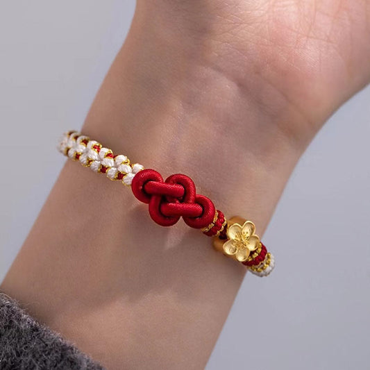 Bracelet porte-bonheur en corde rouge, orné d'un nœud d'amour véritable et d'une fleur de pêcher, selon la tradition bouddhiste tibétaine ancestrale.