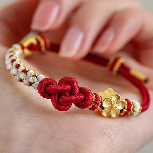 Bracelet porte-bonheur en corde rouge, orné d'un nœud d'amour véritable et d'une fleur de pêcher, selon la tradition bouddhiste tibétaine ancestrale.
