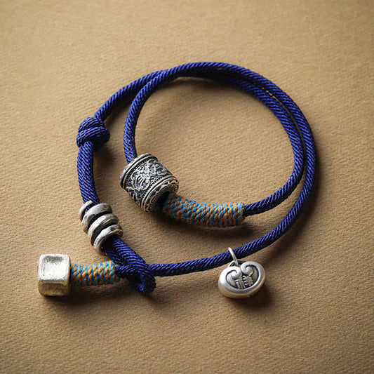 Bracelet à double enroulement en corde rouge, amulette tibétaine traditionnelle, orné d'un Om Mani Padme Hum sculpté à la main, symbole de bon augure et de tradition bouddhiste tibétaine.