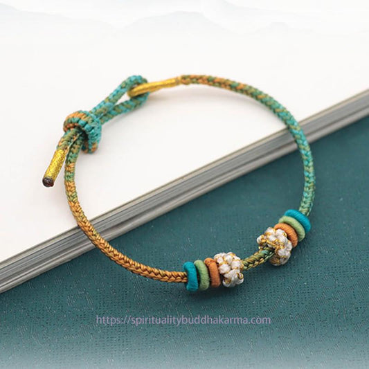 Bracelet tressé à huit fils, orné d'un nœud de fleur de pêcher et d'un nœud rouge, selon la tradition bouddhiste tibétaine ancestrale.
