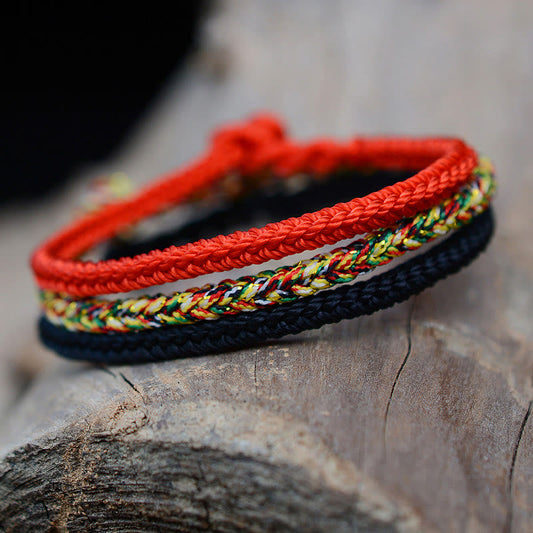 Bracelet tibétain traditionnel à huit fils tressés, orné d'un nœud de paix et de protection, selon la tradition bouddhiste tibétaine ancestrale du fil rouge.