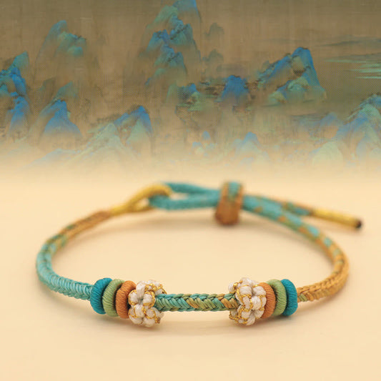 Bracelet tressé à huit fils, orné d'un nœud de fleur de pêcher et d'un nœud rouge, selon la tradition bouddhiste tibétaine ancestrale. 