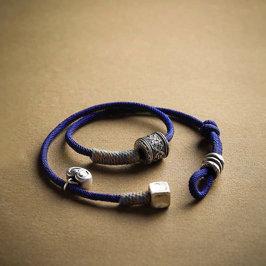 Bracelet à double enroulement en corde rouge, amulette tibétaine traditionnelle, orné d'un Om Mani Padme Hum sculpté à la main, symbole de bon augure et de tradition bouddhiste tibétaine. 