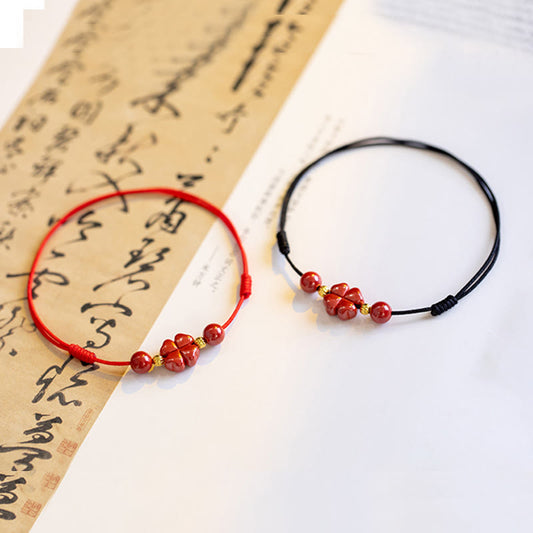 Alte tibetisch-buddhistische Tradition: Armband und Fußkettchen aus rotem Faden mit vierblättrigem Kleeblatt und Zinnobermotiv – ein Segen für Ruhe und Gelassenheit. 